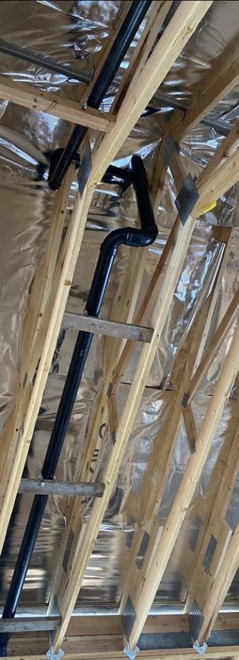 Exposed timber roof rafters lined with reflective insulation, with a black ventilation duct running between the beams in an unfinished attic.